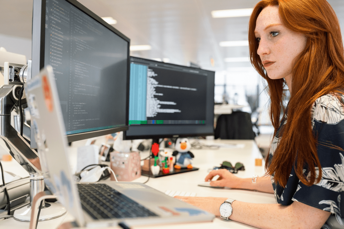A woman working at a desk with several screens all showing source code 