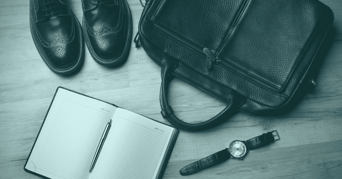 A pair of black school shoe on the floor next to an open notebook, a watch and a school bag